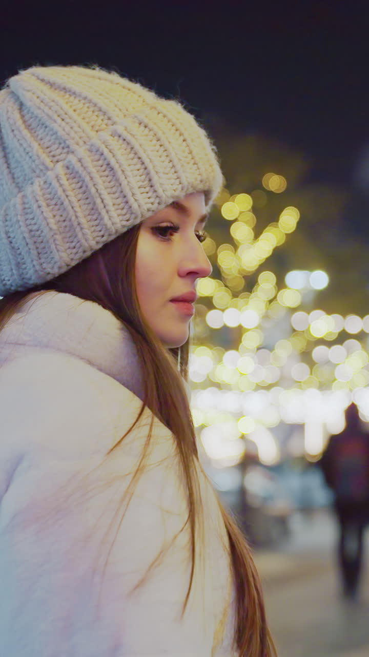 Woman in winter outfit and knitted beanie walking through vibrant city streets at night, surrounded by glowing festive lights and bokeh effects