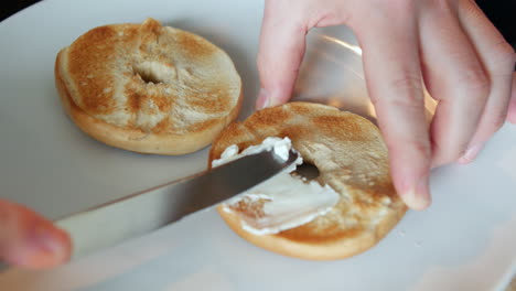 untar queso crema en un bagel con un cuchillo