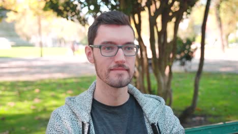 young man glasses sitting on park bench staring in distance