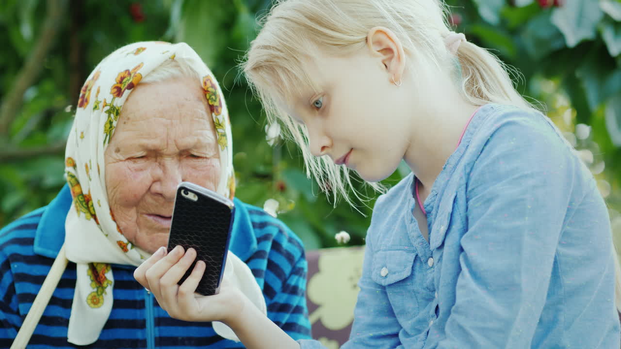 그 소녀는 세대 개념 4k 비디오의 스마트폰 친교에 할머니 사진을 보여줍니다