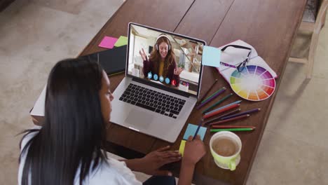 african american female teacher writing on memo notes having a video call on laptop at home