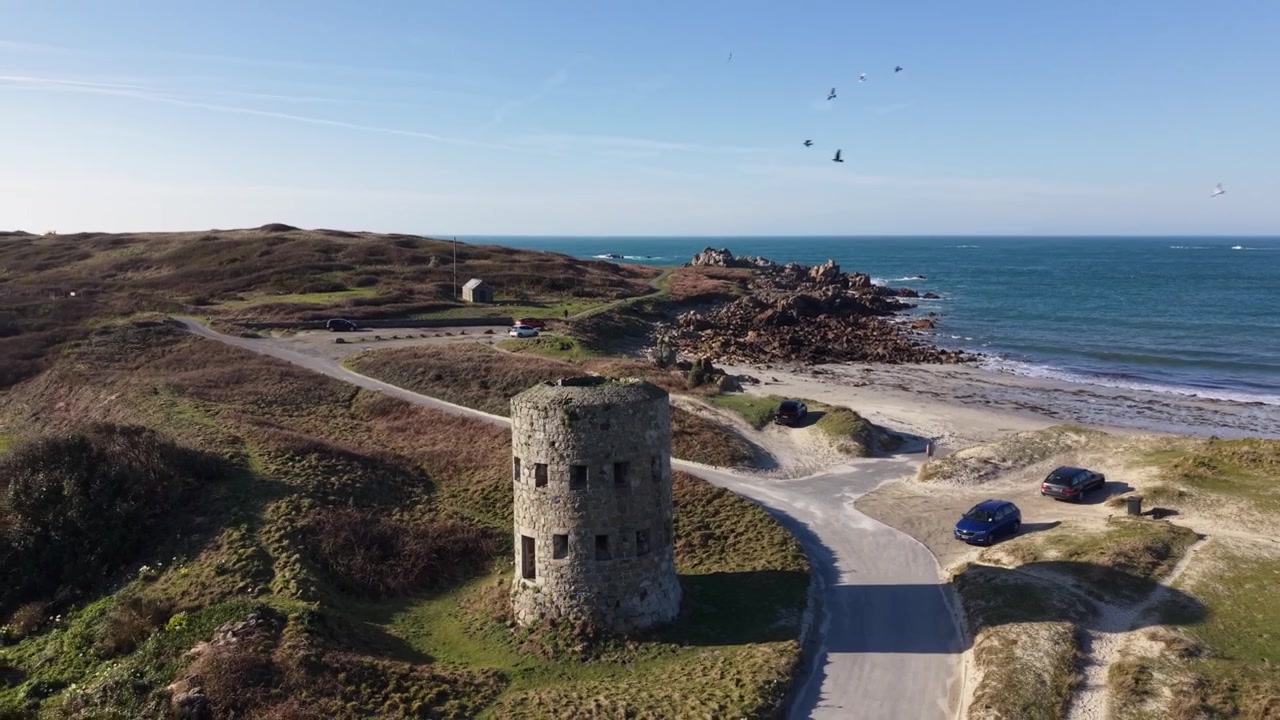 Torre Martello Pembroke Vale Guernsey. Rivelazione della torre dall'alto con vista sulla spiaggia di Jaonneuse, uccelli in volo e vista sul mare nel sole del tardo pomeriggio