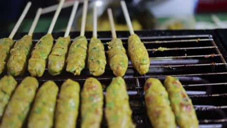 Tilt-down-shot-of-food-vendor-preparing-and-cooking-Thai-styled-grilled-fish-cake-with-herbs-on-skewers-on-hot-flaming-charcoal-grill