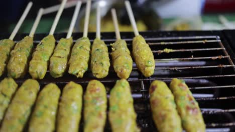 disparo inclinado hacia abajo de un vendedor de alimentos preparando y cocinando un pastel de pescado a la parrilla al estilo tailandés con hierbas en pinchos en una parrilla de carbón caliente.