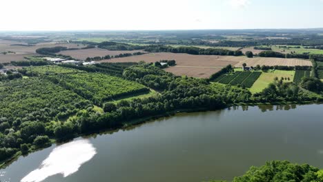 Grain-fields-and-forest-surrounding-Vallum-lake-at-Djursland-close-to-Aarhus-in-Denmark---Aerial