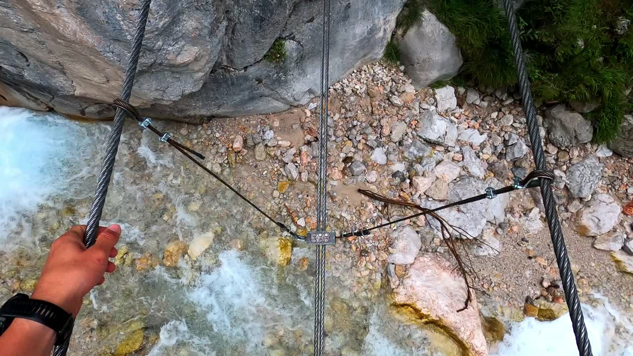 toma pov de un hombre balanceándose a través de un río cristalino en un puente de cable de acero