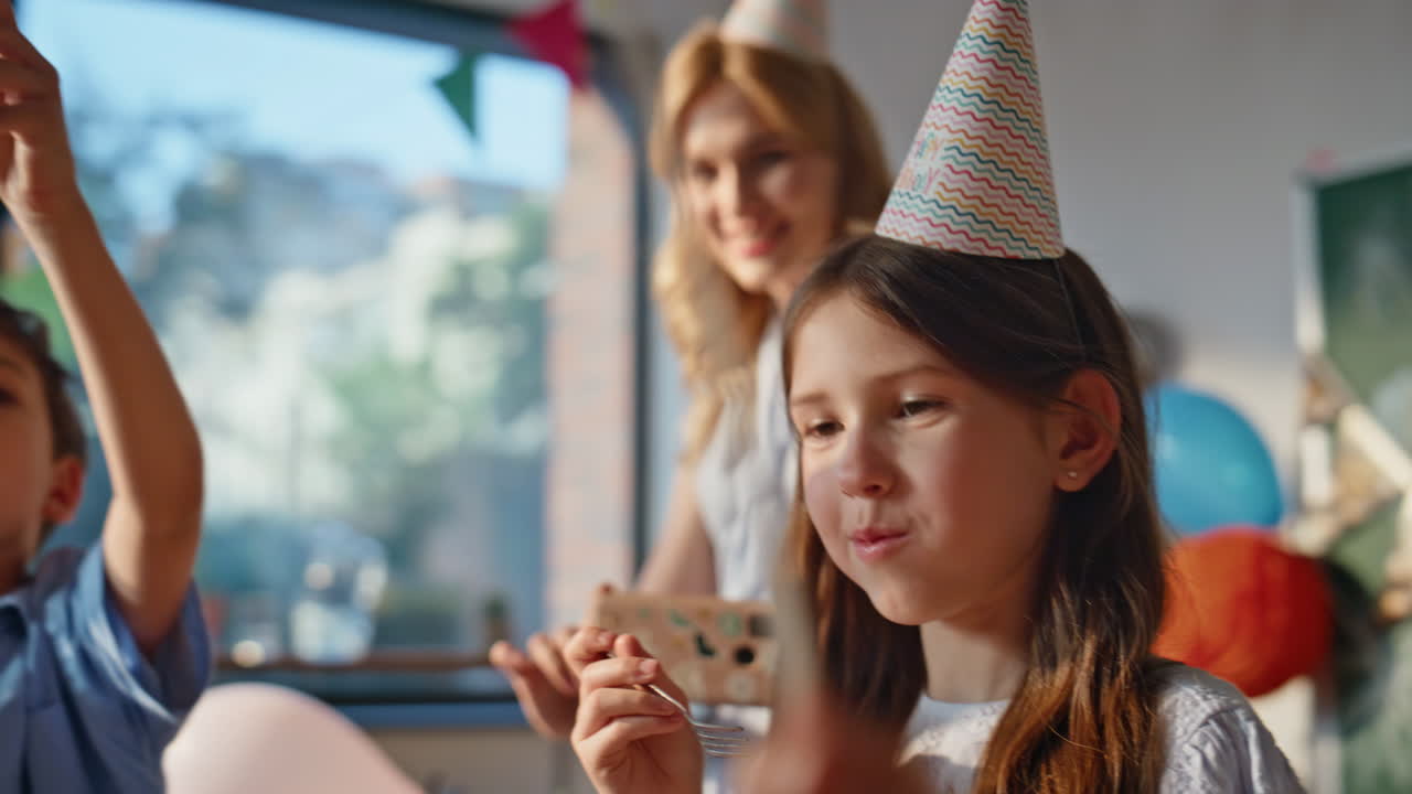 Birthday girl eating cake at school celebration with classmates closeup