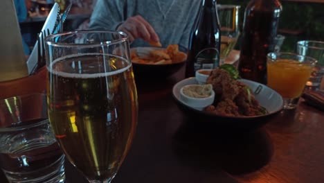 un primer plano de un vaso de sidra con una mujer comiendo comida en el fondo