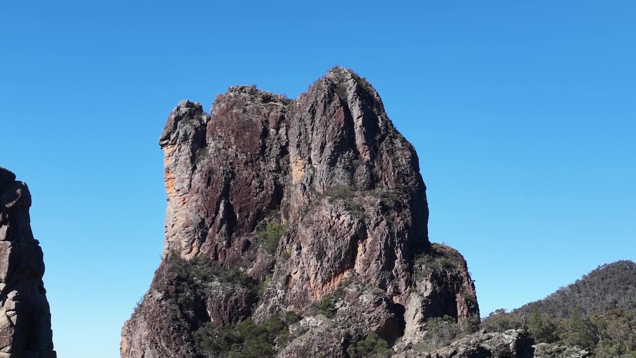 Panorering af gamle vulkanske tinder under en klar blå himmel i Warrumbungle Nationalpark.