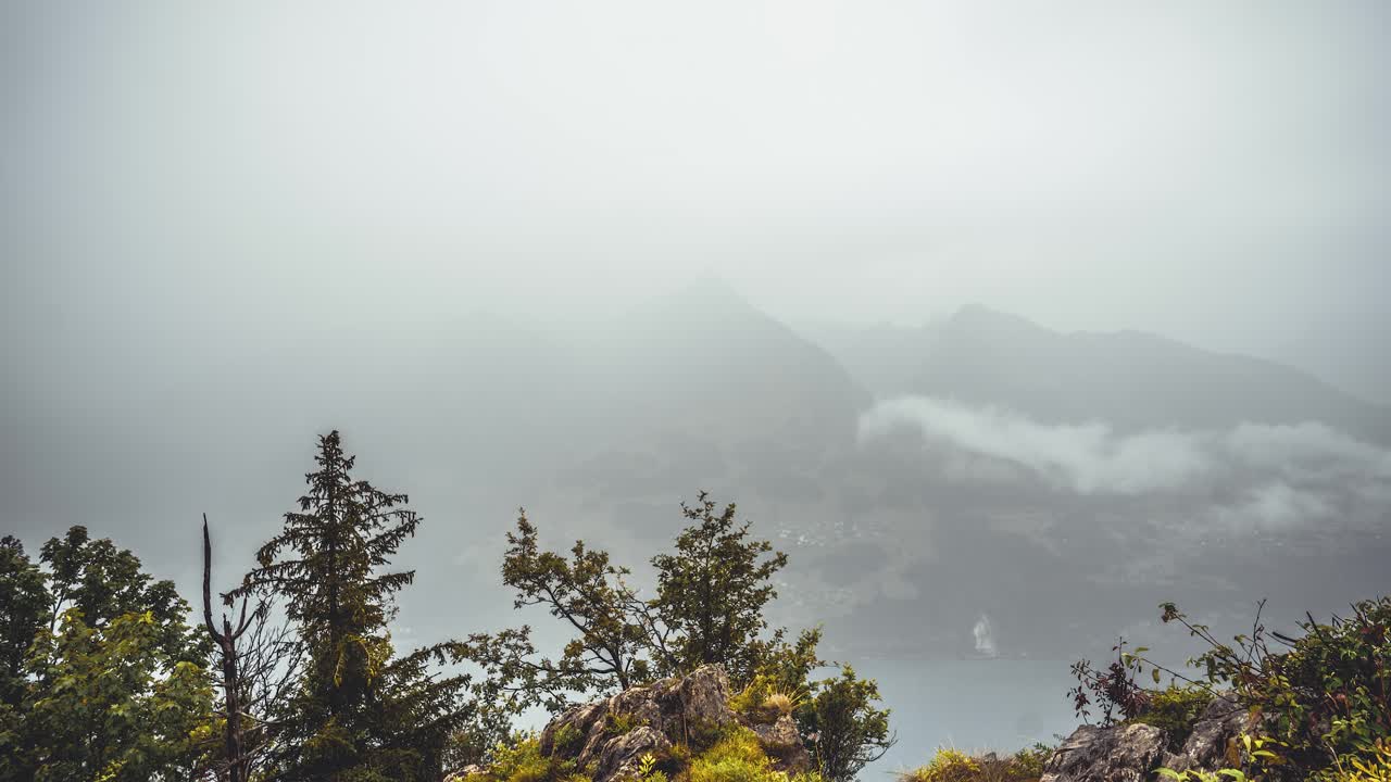 Thick rain clouds blankets the peaks near Amden (St. Gallen, Switzerland). Moving fog creates a mystical, alpine atmosphere. Faint village outlines can be seen through the mist. (moving timelapse)