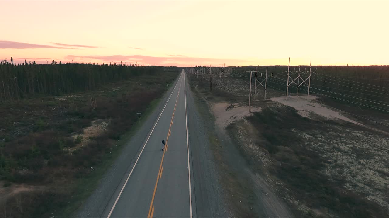 un tipo patina en un largo camino durante una puesta de sol de verano