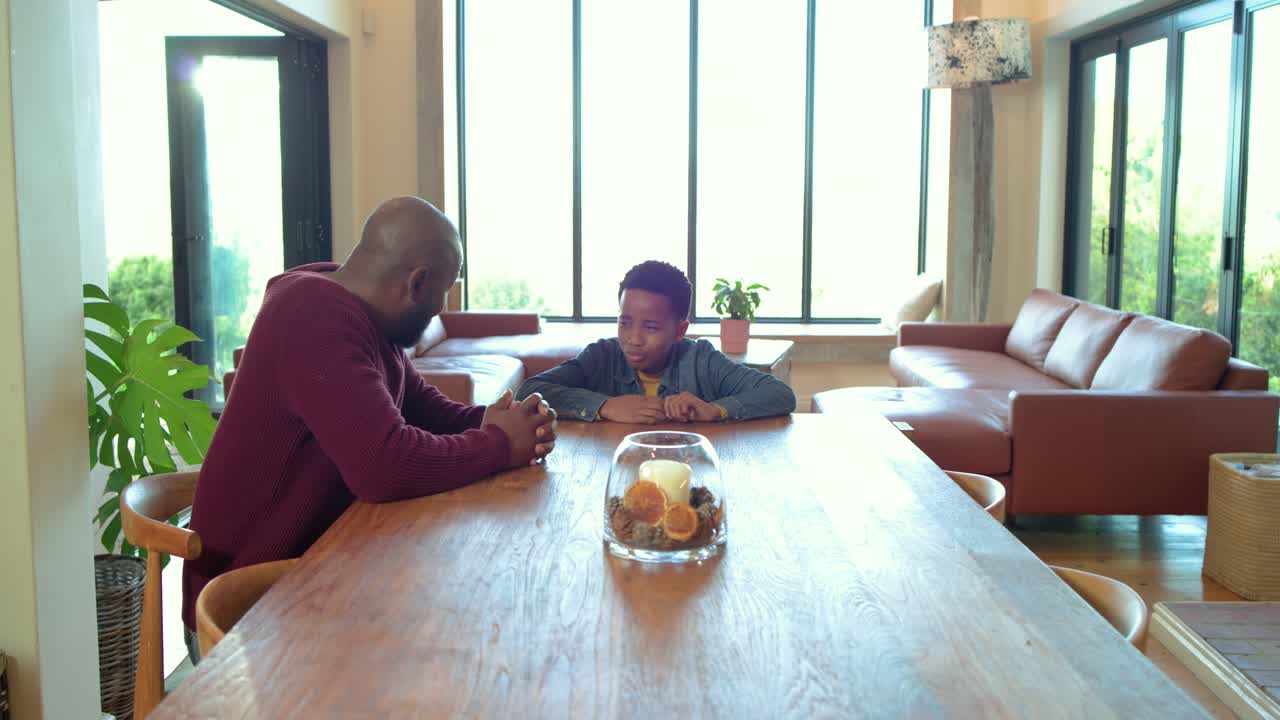 African American father preteen son talking at dining table as camera pulling back revealing candle