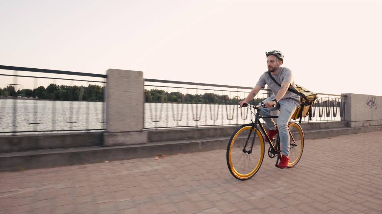열 배낭을 착용한 음식 배달 라이더 남자는 강 옆에서 자전거를 타고 고객과 고객을 위한 주문을 배달합니다.