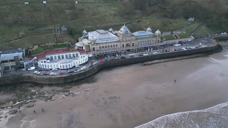 cinematic shot of scarborough spa with cars parked in front of it and a beautiful beach with small tides in it in scarborough, england