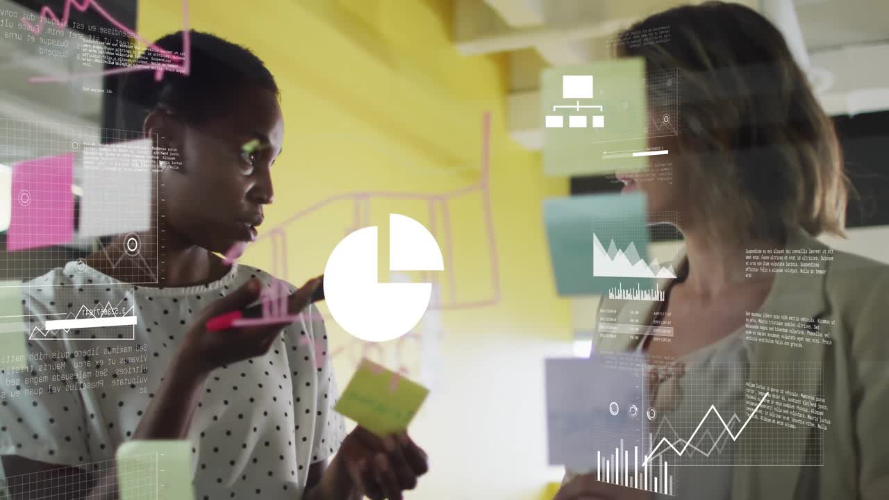 Two mid adult women adding sticky notes at glass partition, brainstorming business plan with charts