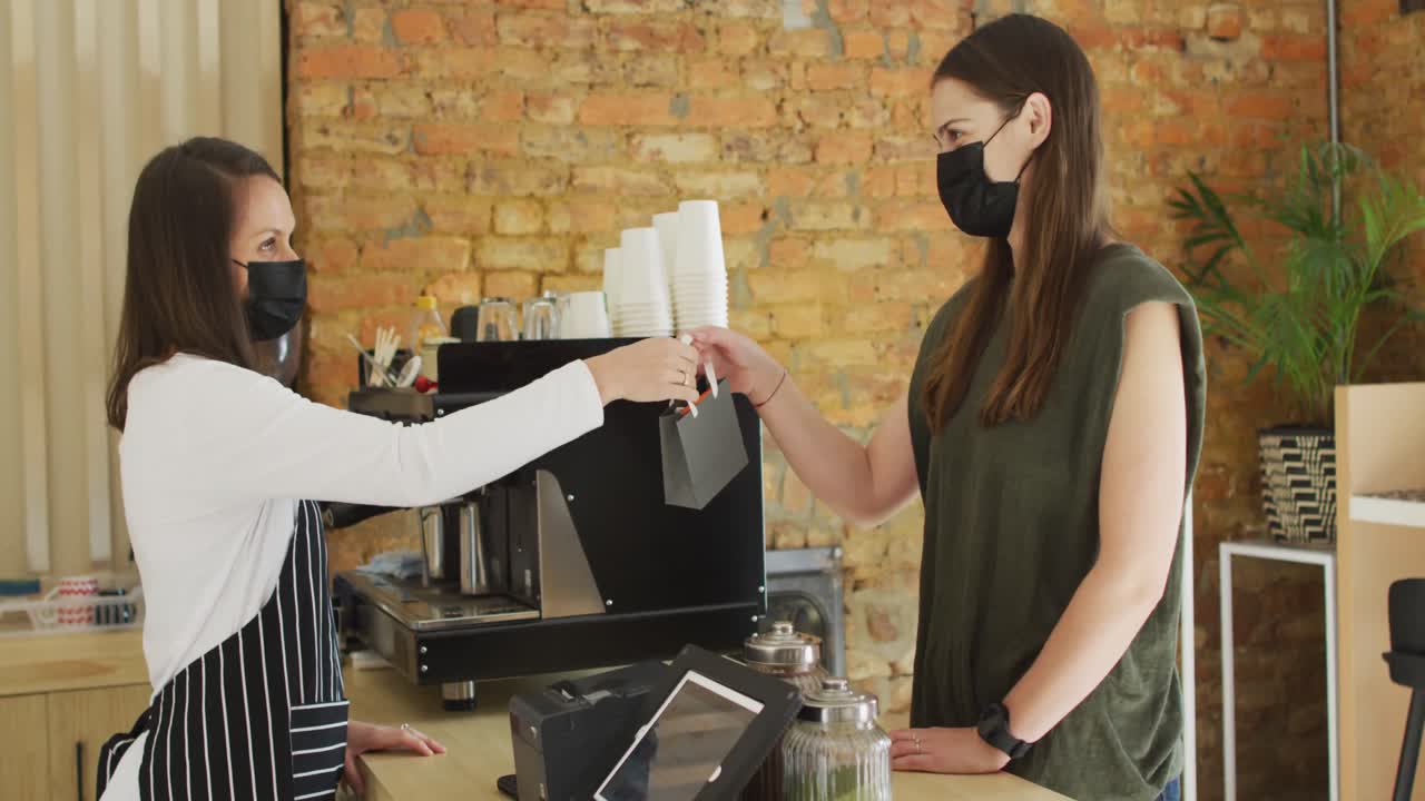얼굴 마스크를 쓴 백인 웨이트리스가 백인 여성 고객에게 테이크 어웨이 주문을 하고 있습니다.