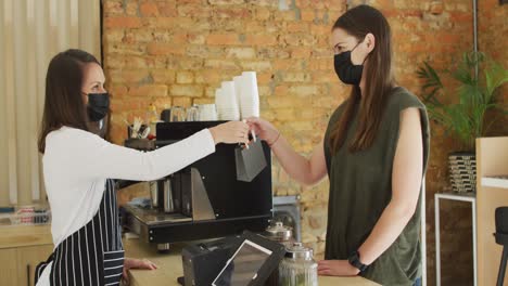 camarera caucásica con máscara facial dando un pedido de comida para llevar a una cliente caucásica