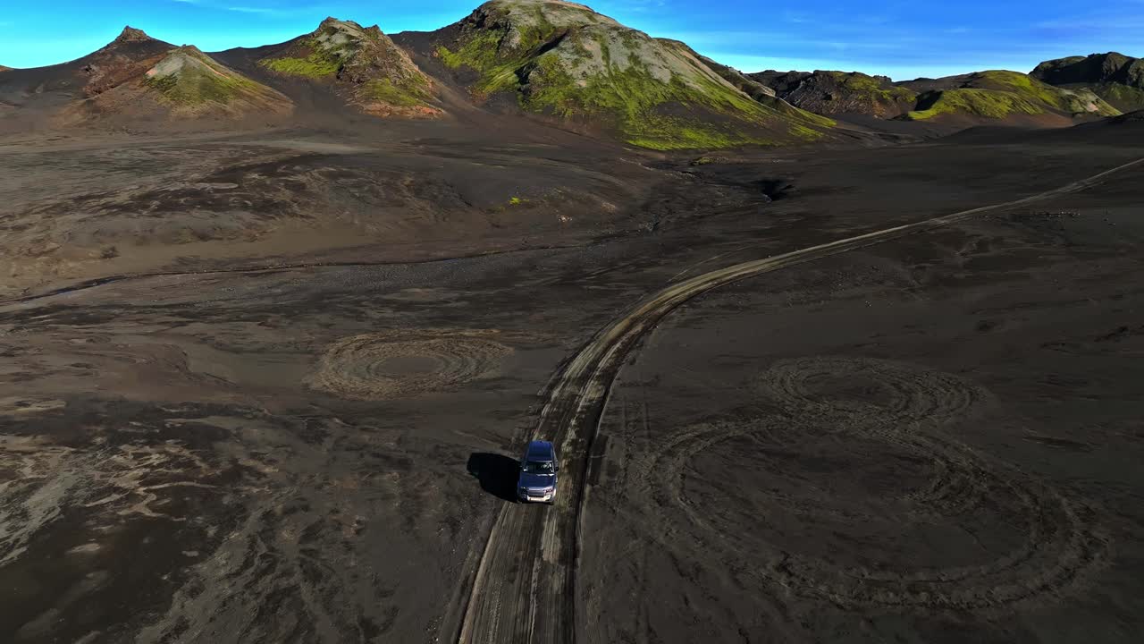 Vista aerea di un'auto che percorre una strada sterrata attraverso un paesaggio vulcanico