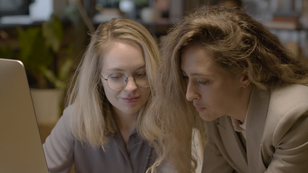 dos empleadas mirando algo en el teléfono móvil y hablando juntas mientras trabajan en la oficina 1