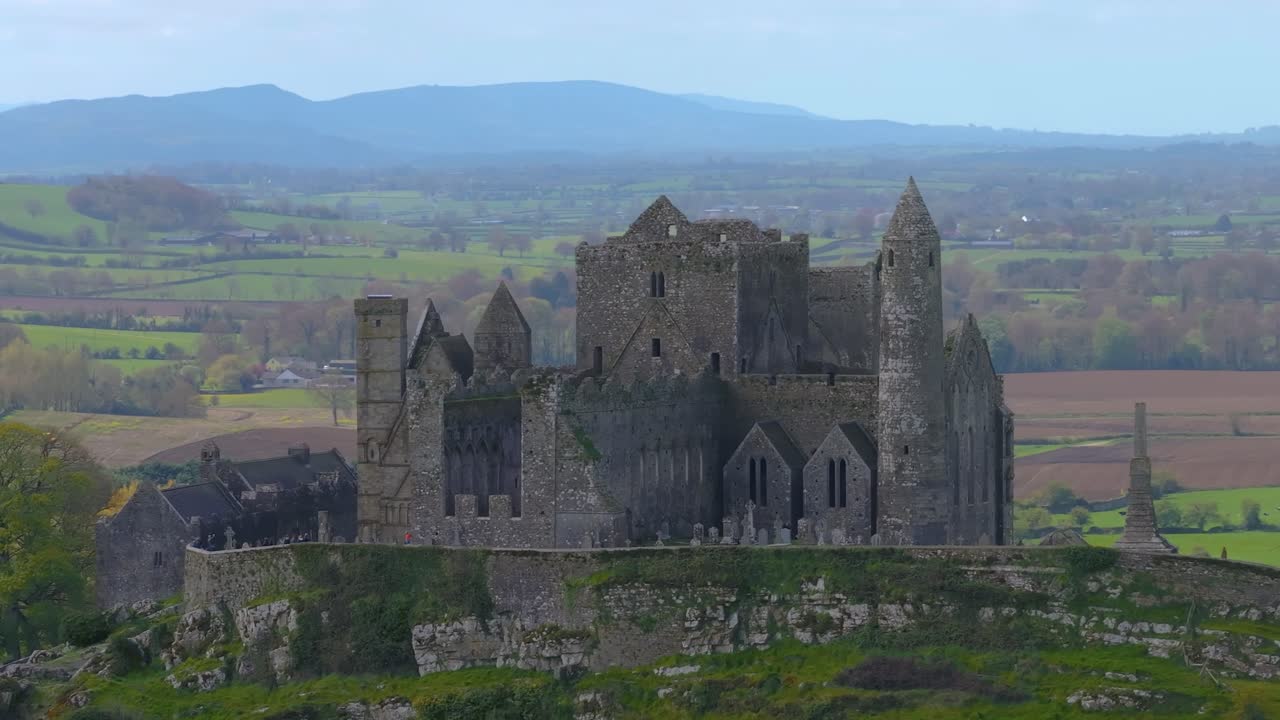 4K Aerial view of the Rock of Cashel, capturing ancient stone walls, round towers, and cathedral ruins surrounded by rolling green fields and historic farmland. Co.Tipperary, Ireland_06