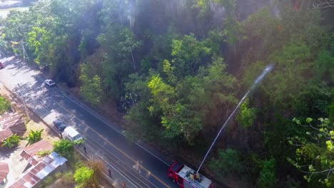 Aerial-view-of-a-fire-truck-using-a-hose,-to-extinguish-of-wildfire,-in-a-tropical-forest---rising,-pull-back,-drone-shot