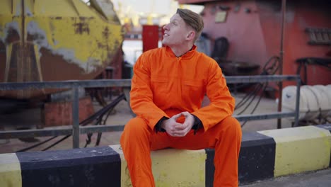 Junger-Mann-In-Orangefarbener-Uniform-Sitzt-Während-Seiner-Pause-Am-Meer-Im-Hafen