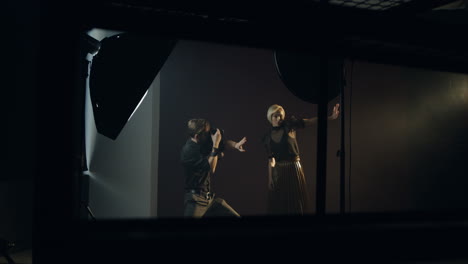 사진 작가가 그녀의 사진을 찍는 동안 어두운 스튜디오에서 포즈를 취하는 백인 젊은 여성 모델의 먼 전망