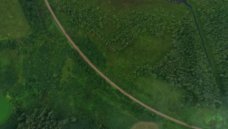 High-aerial-drone-shot-over-lake-surrounded-by-dense-green-vegetation-on-a-cloudy-day