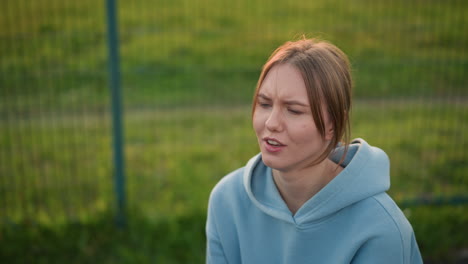 close-up of lady with hair tied back playing volleyball, focusing on training session, she attempts to catch the ball as it flies, with an open field and bar fence in background behind her