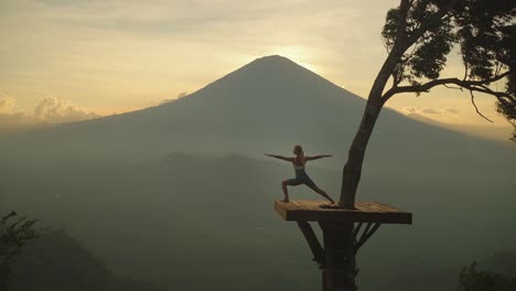 Mujer-En-La-Plataforma-Balinesa-De-Lahangan-Dulce-Haciendo-Pose-De-Guerrero-Con-Vista-Al-Volcán-Agung,-Puesta-De-Sol