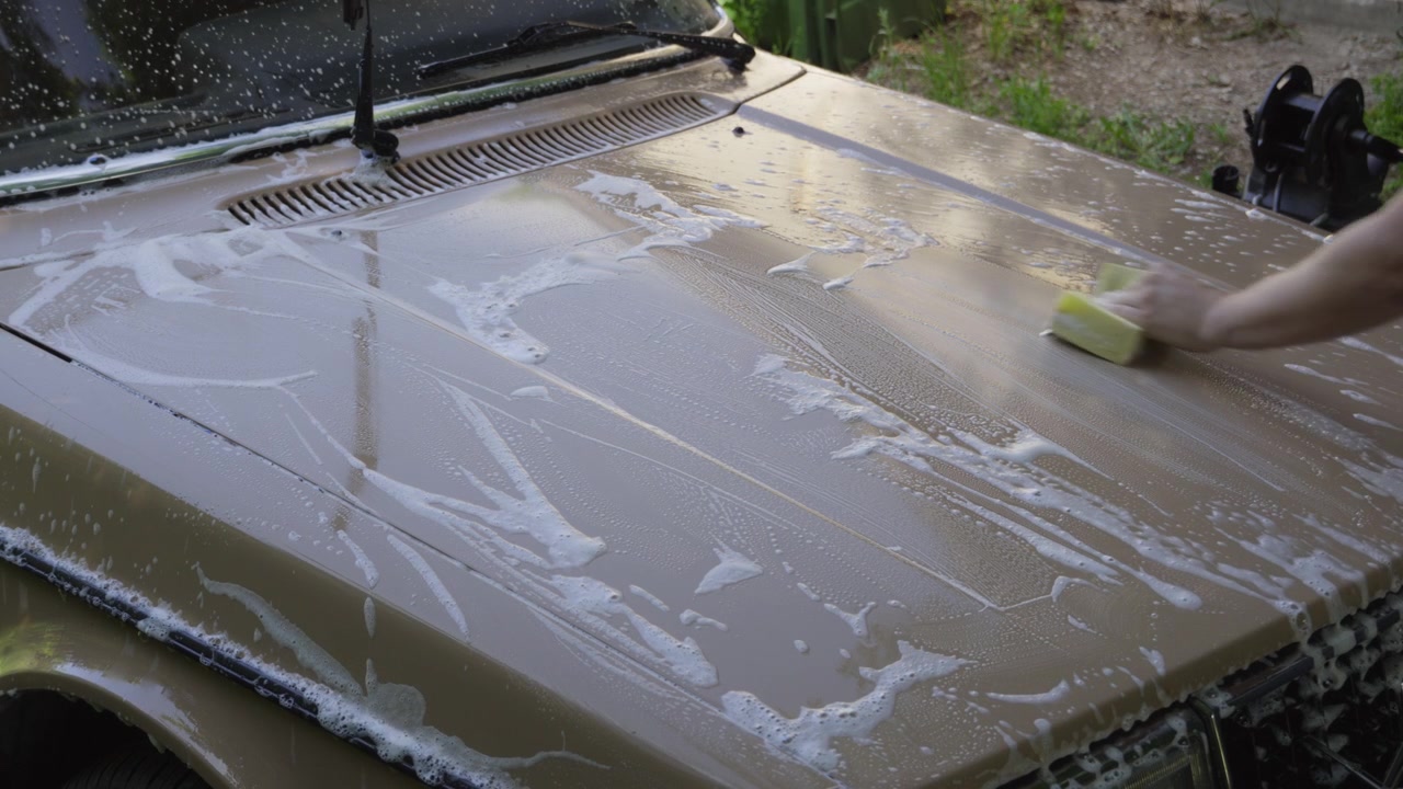 A person hand washes a vintage car hood with soapy water at home. Ideal for classic car restoration, car care, detailing and automotive lifestyle content.