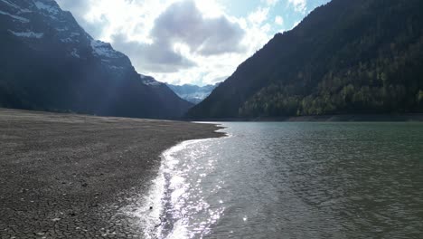 Aerial-forward-view-of-shoreline-of-an-alpine-lake-in-a-fantastic-mountain-landscape