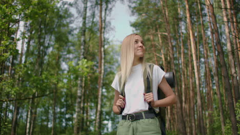 handheld shot of thoughtful serious female hiker with backpack walking amidst trees in forest. a young woman with a backpack walks through the forest on a summer day.