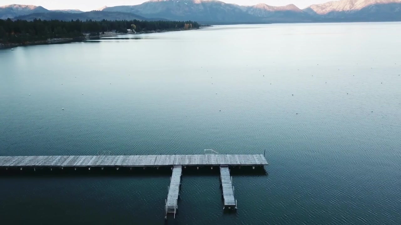 This video is capturing a long dock reaching out into a calm lake on an early morning.