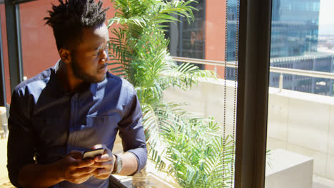 Vista-Frontal-De-Un-Joven-Empresario-Negro-Usando-Un-Teléfono-Móvil-En-Una-Oficina-Moderna-4k