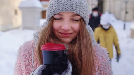 girl tourist with hot drink in cup looking around through street in town during holiday vacations