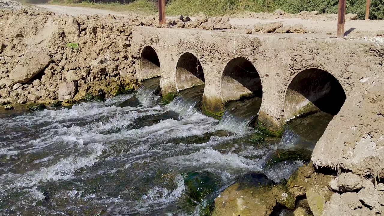 Rustic culvert bridge with water gushing through its arches into lively stream, nature, rural infrastructure and environment.