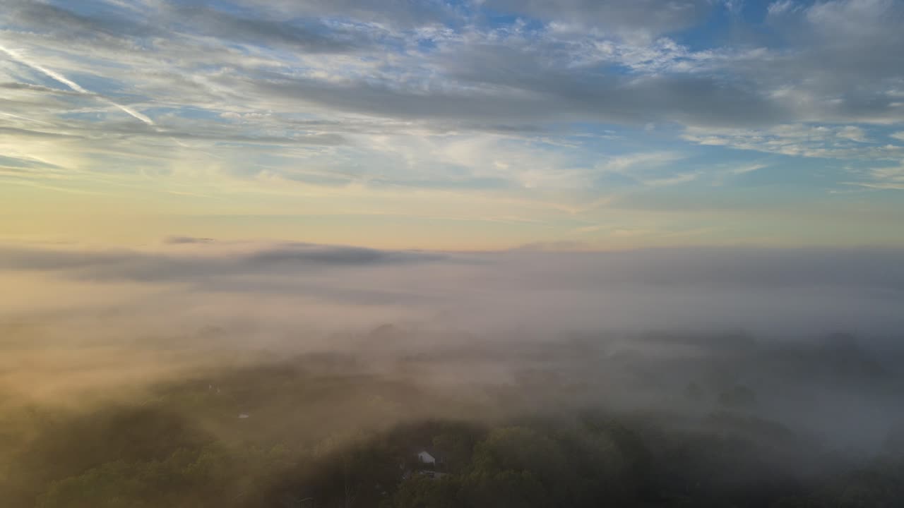 The camera drone is rising from quiet little town streets through the fog clouds to reveal a blanket of fog. 4k 30fps.