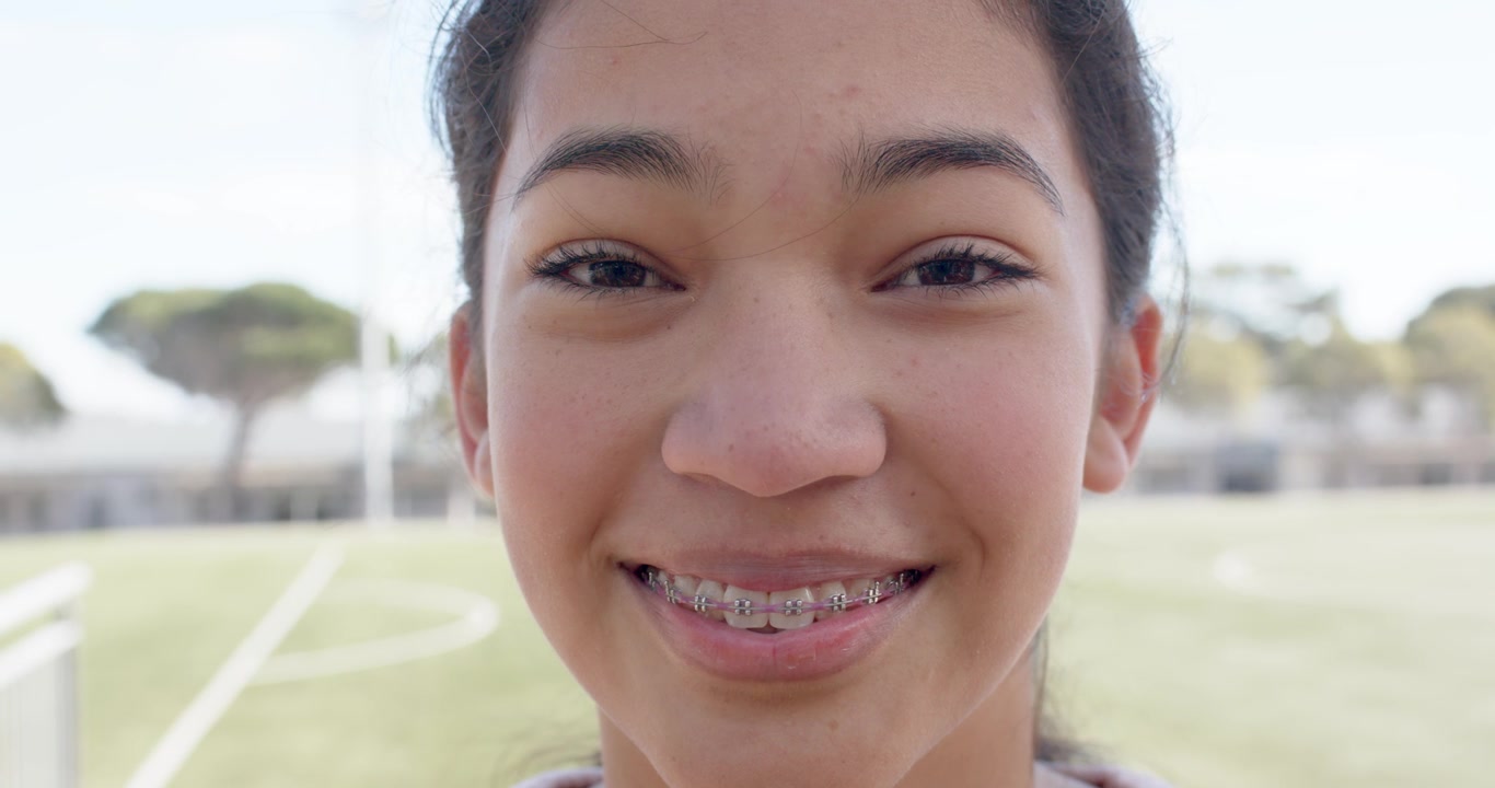 African American teen closing eyes, opening, smiling, showing braces in sports top on grass pitch
