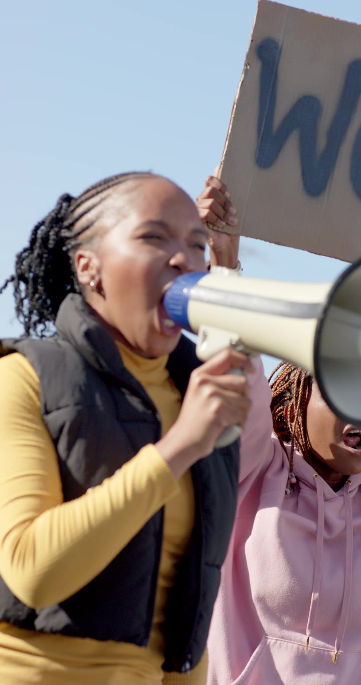 Video verticale: Donne manifestanti africane che usano un megafono mentre reggono un cartello "WOM" durante una manifestazione.