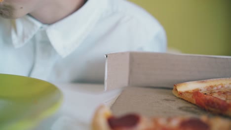 schoolboy eats pizza with sausage and tomatoes at table