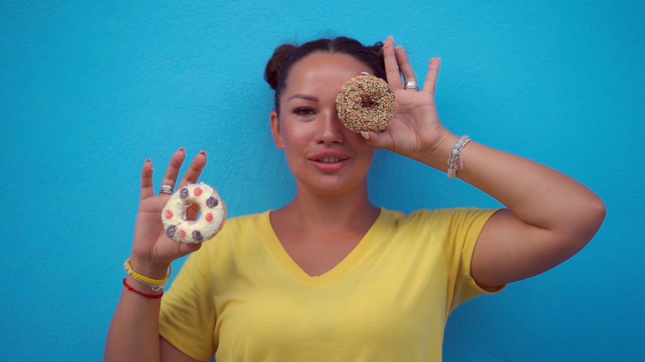 Young Woman Holding Donuts Over Her Eyes Against Blue Background