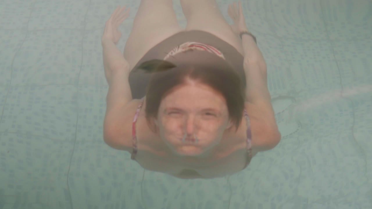 una joven pelirroja saca la cabeza de una piscina y sonríe a la cámara