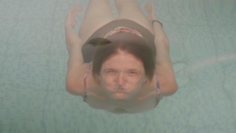 una joven pelirroja saca la cabeza de una piscina y sonríe a la cámara