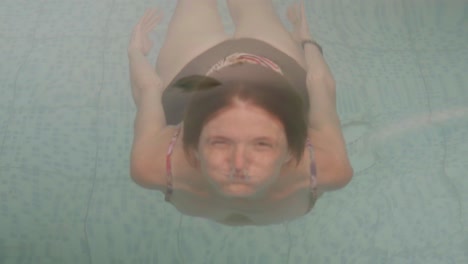 a young redhead water sticks her head out of a swimming pool and smiles at camera