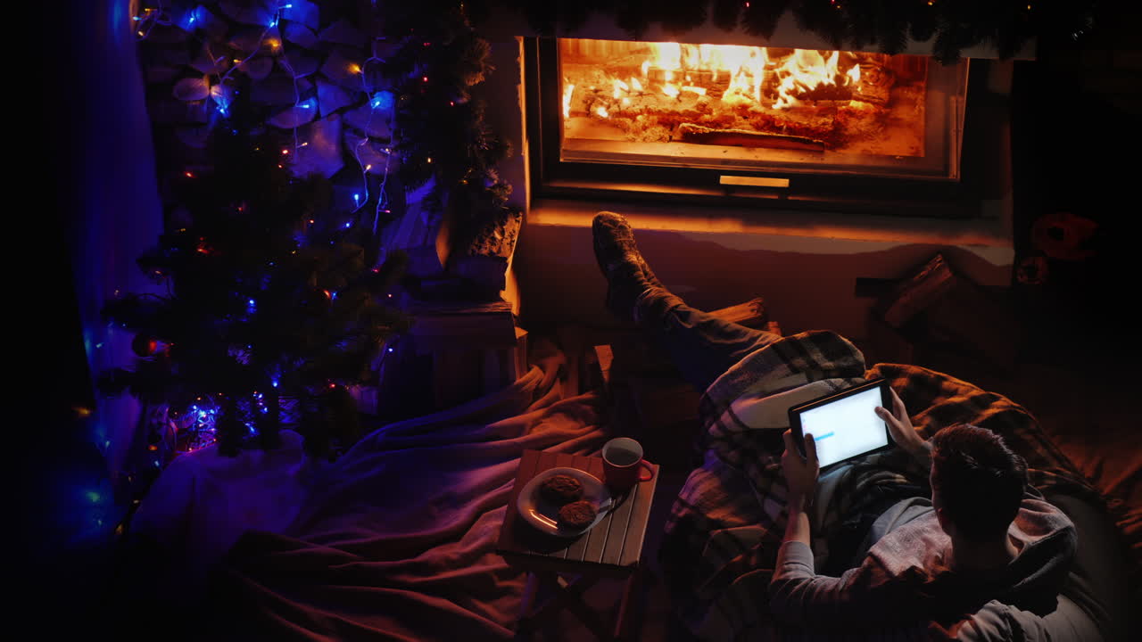 vista superior un hombre usa una tableta junto a la chimenea y el árbol de navidad ordenando regalos navideños