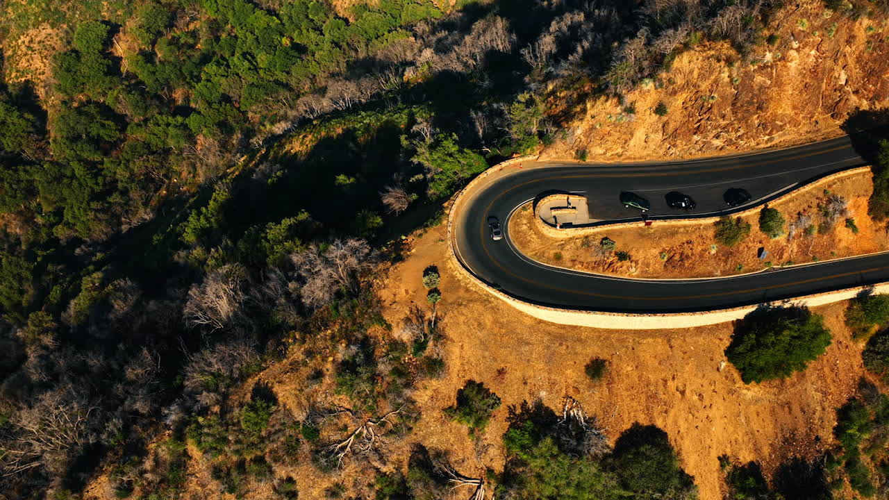 Loop on the highway on the rock. Car goes by the road over the green wood growing on the slopes. Aerial view.