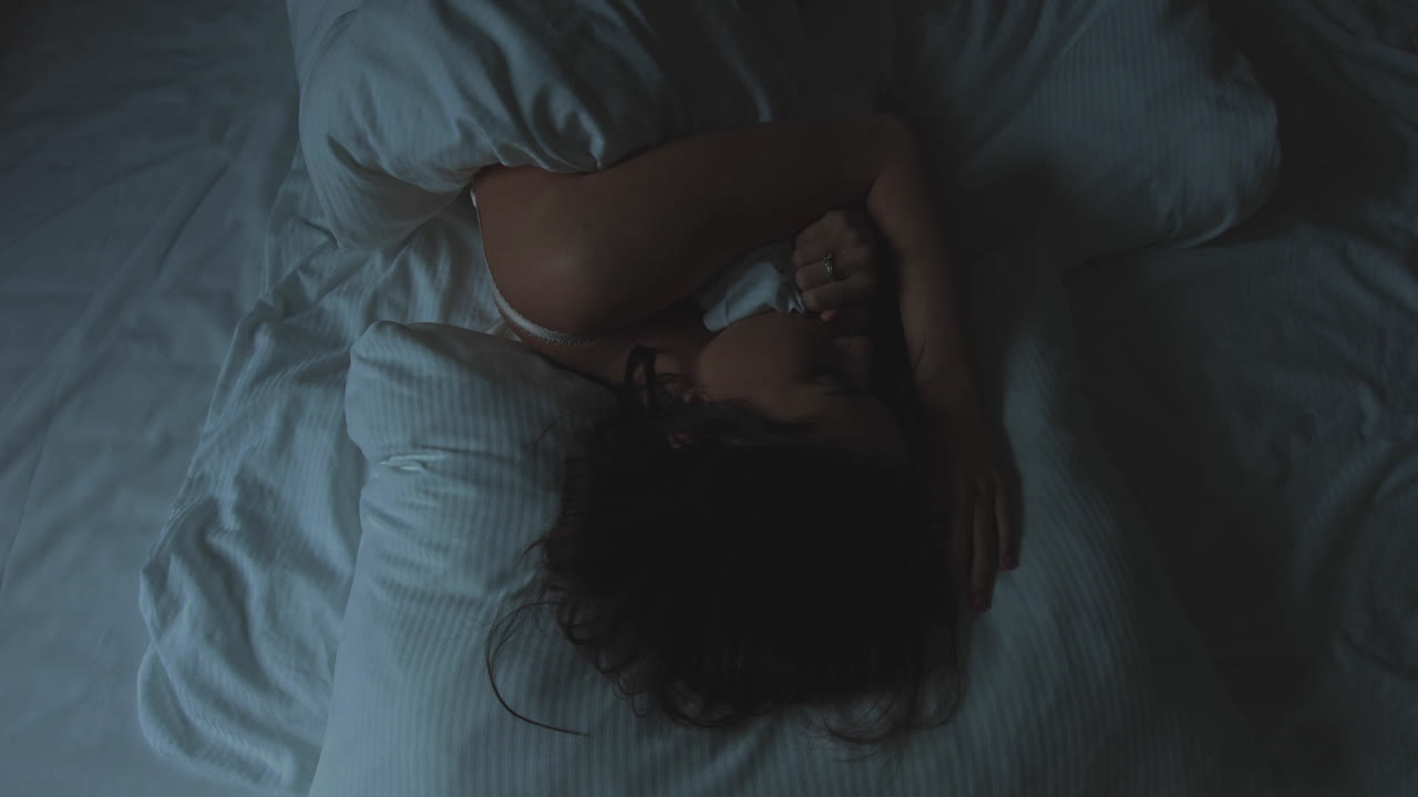 The young woman lies in bed and cannot sleep. It moves from side to side. She is restless and nervous. He has nightmares. He suffers from insomnia. The woman is sick and nervous. Sleepless night