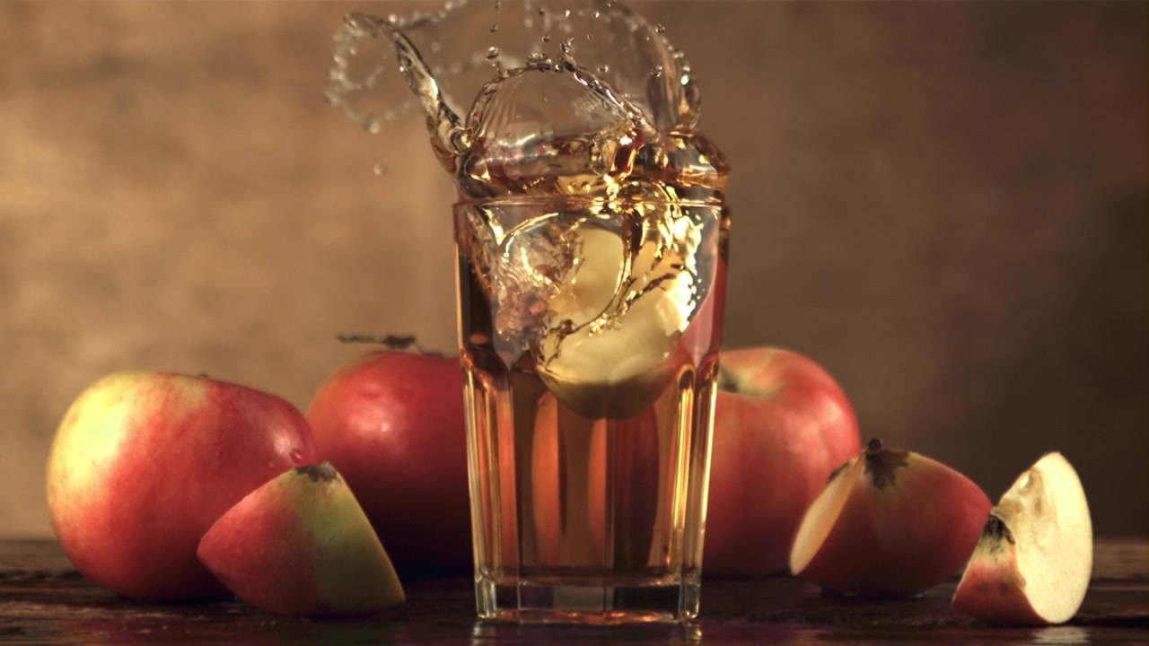 Rallentatore di una fetta di mela che cade in un bicchiere di succo.