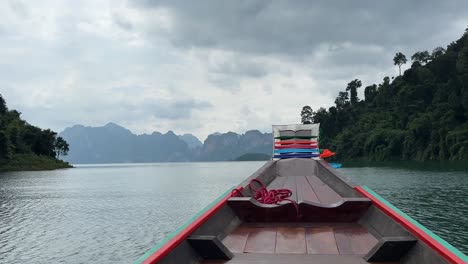 Gliding-on-a-long-tail-boat-on-Thailand's-Khao-Sok-Lake,-Boat's-front-adorned-with-colorful-fabric-at-its-tip